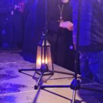 Mustaan kaapuun pukeutunut pappi jakaa joulutulta lyhtyihin