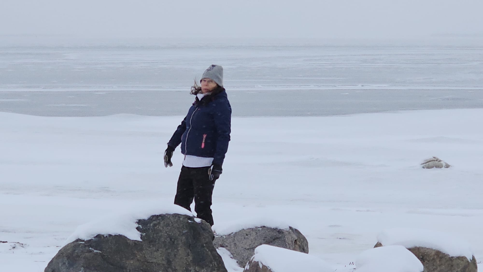 Nainen seisoo jäätyneen meren rannalla suuren kiven takana