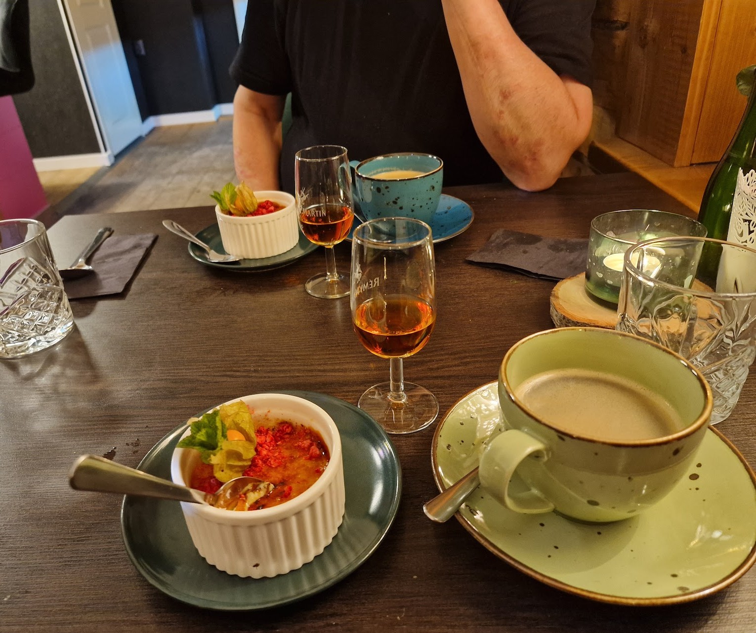 Ravintolan pöydässä kaksi kahvikuppia ja konjakkilasia sekä makea jälkiruoka pienessä pyöreässä kipossa